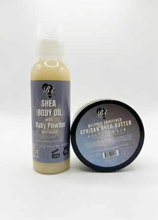 A bottle of Shea Body Oil with Baby Powder and a round tub of Whipped Unrefined African Shea Butter Baby Powder, both with matching labels, displayed on a clean white background.
